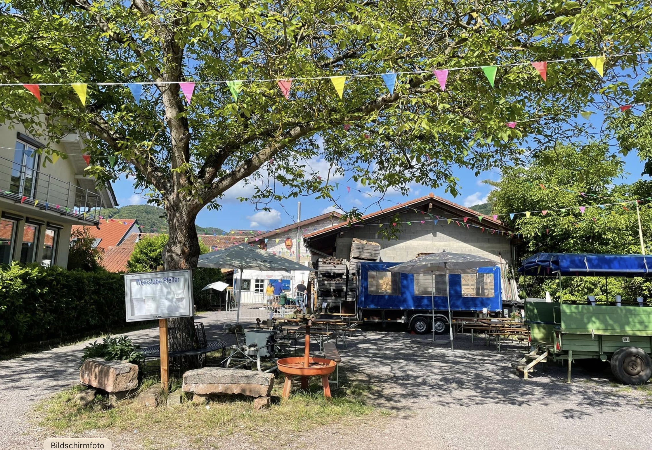 Blick auf die Rückseite des Weinhofs mit großem Baum, Hoftischen und Planwagen