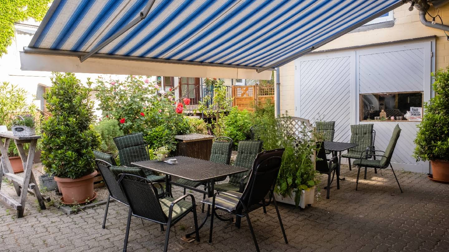 Sitzplätze im begrünten Hof unter der blau-weißen Markise